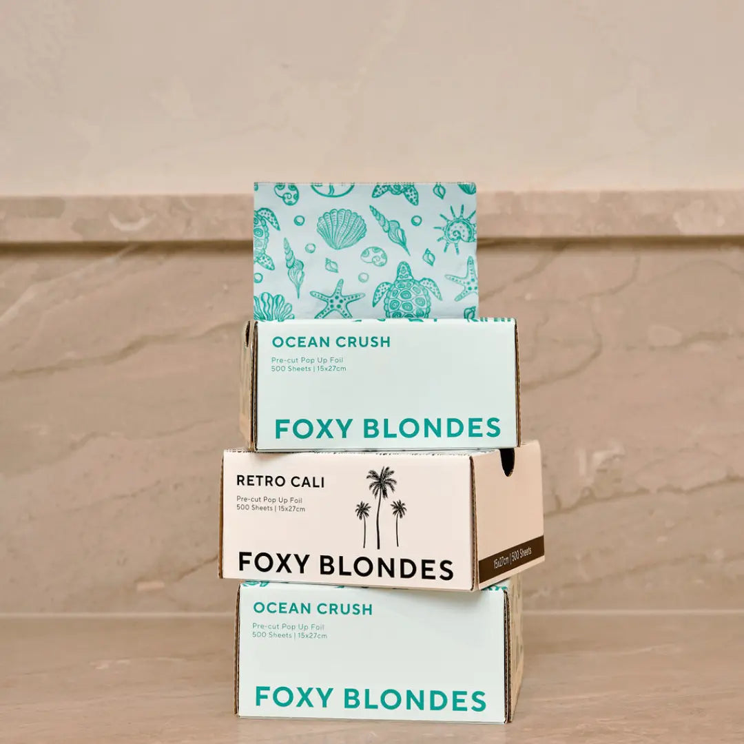 Stack of three Foxy Blondes pre-cut pop-up hair foil boxes: 'Ocean Crush' (sea life print, top and bottom) and 'Retro Cali' (palm tree print, middle), with an Ocean Crush foil dispensing.