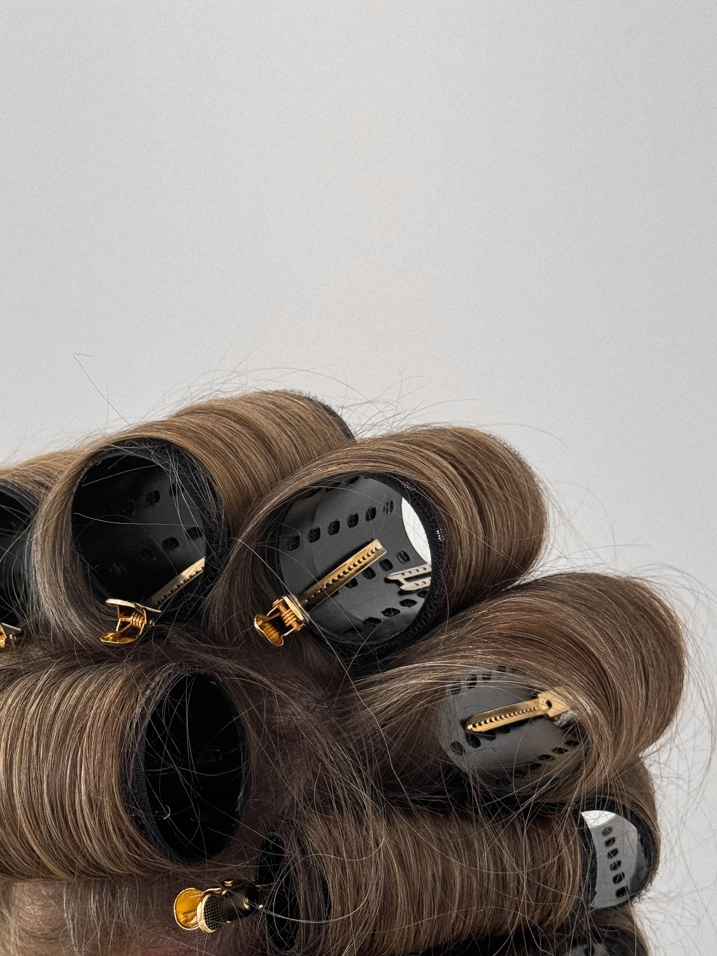 Set of hair rollers with brown hair on a light gray background